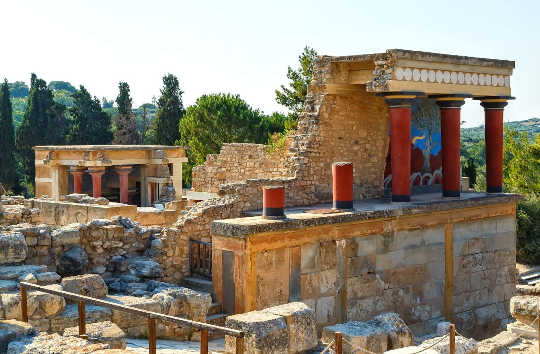 Ruins of the Minoan Palace of Knossos in Crete, with its iconic red columns and frescoes in the background.