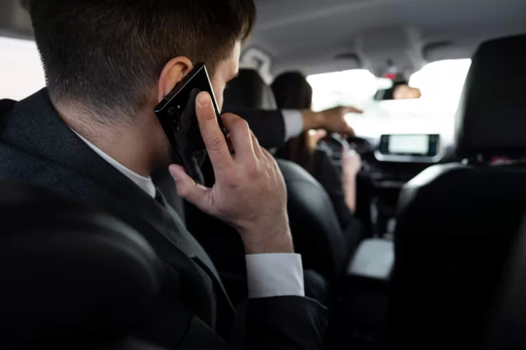 Passenger in a suit talking on the phone inside a taxi, while the driver is driving.