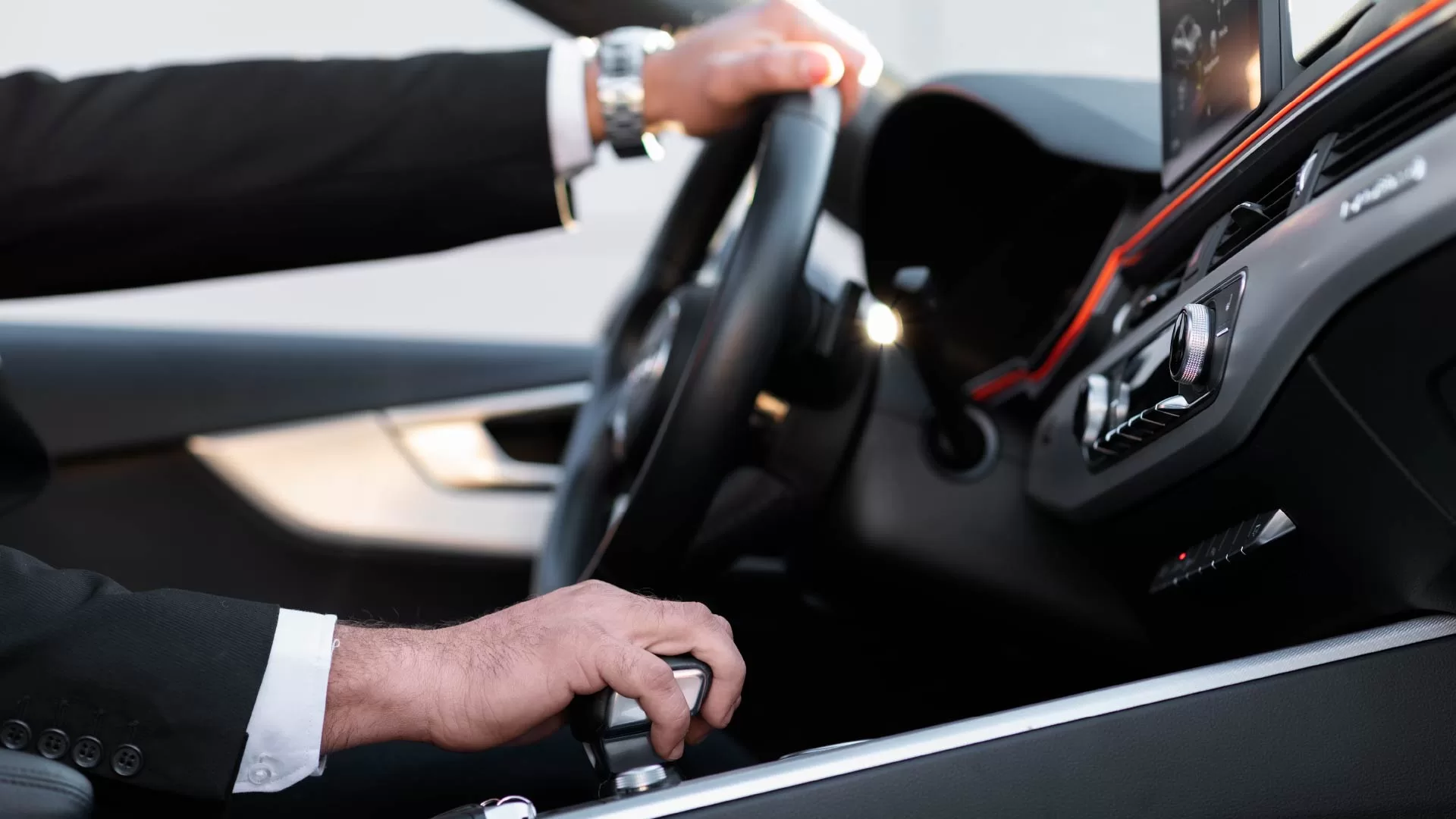 Chauffeur in a suit behind the wheel of a luxury vehicle, ready to transport guests.